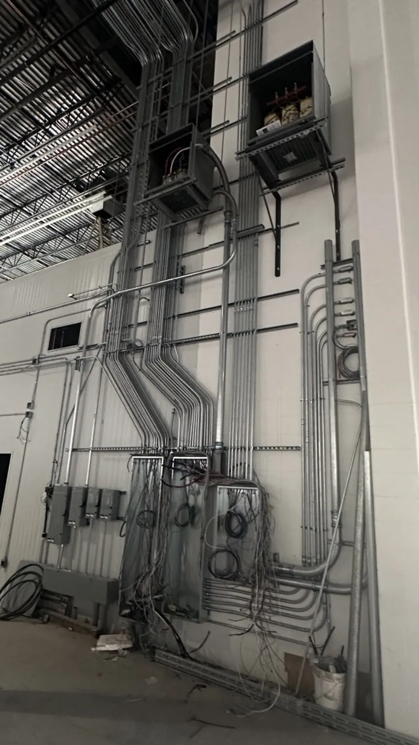 Commercial electrical and low-voltage conduit rough-in on a high-bay wall